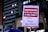 A poster is being held up at a protest. It contains Portuguese text advocating for democracy and rejecting amnesty. The background shows a cityscape with lit buildings and a traffic light.