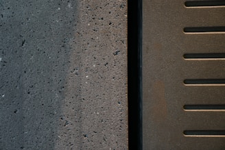 A close-up view of two adjacent surfaces, one concrete with small holes and a textured pattern, and the other metal with parallel slotted lines.