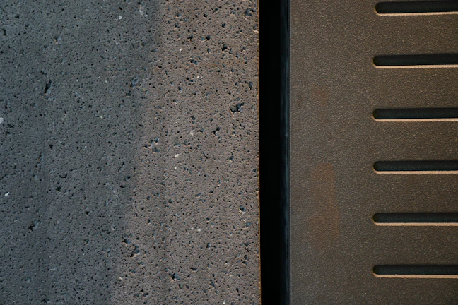Close-up of textured raw concrete surface juxtaposed with smooth black metal detailing.