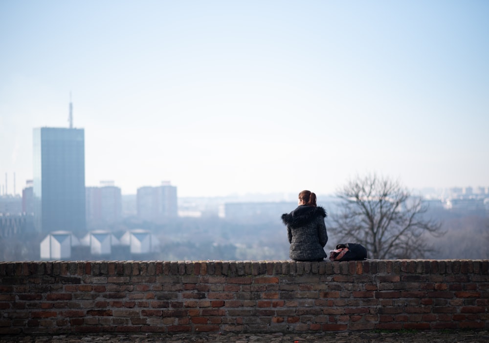 a person sitting on a brick wall with a city in the background