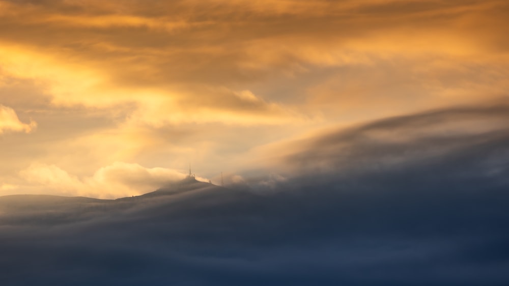 a bird flying through a cloudy sky with a mountain in the background