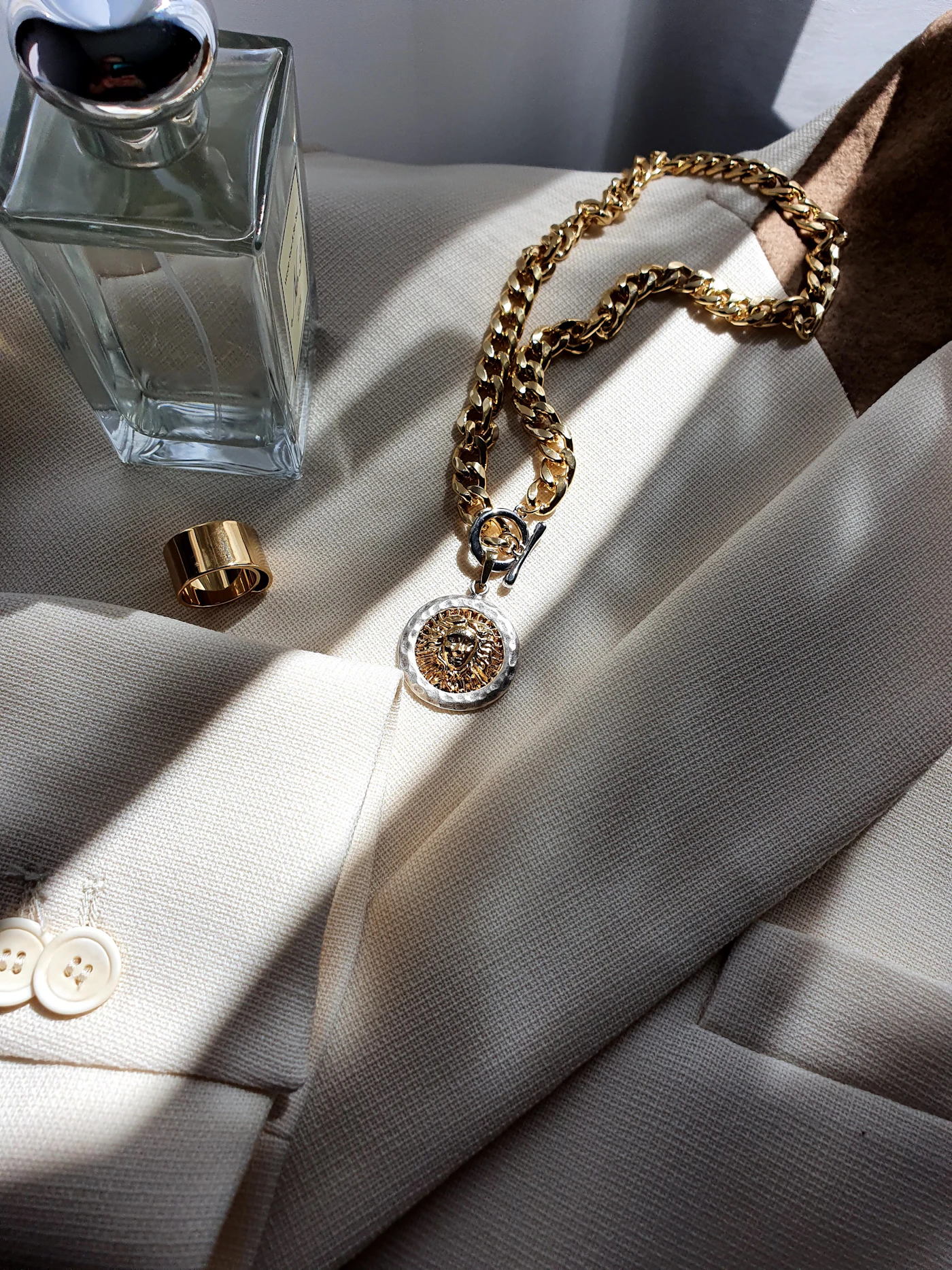 Perfume, jewelry and a cream blazer arranged in sunlight