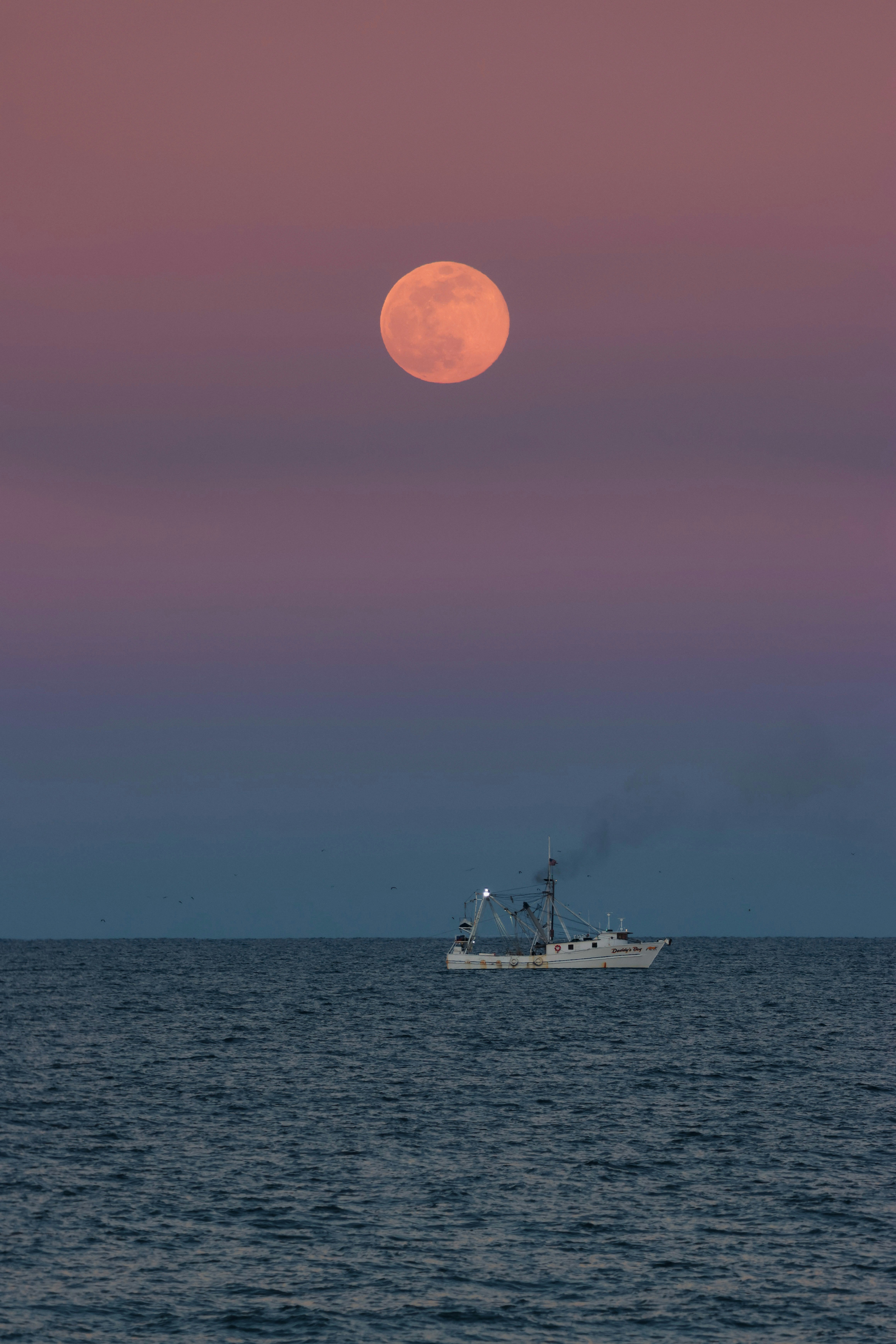 a boat in the ocean with a full moon in the background