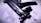 A close-up view of a sleek, black submachine gun placed on a textured surface. The image highlights the weapon's intricate details and matte finish under dramatic lighting, casting shadows and enhancing its features.