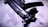 A close-up view of a sleek, black submachine gun placed on a textured surface. The image highlights the weapon's intricate details and matte finish under dramatic lighting, casting shadows and enhancing its features.