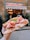 A hand holds a large, freshly made sandwich filled with thinly sliced ham, cheese, and arugula, with a backdrop of a bustling deli entrance and its sign.