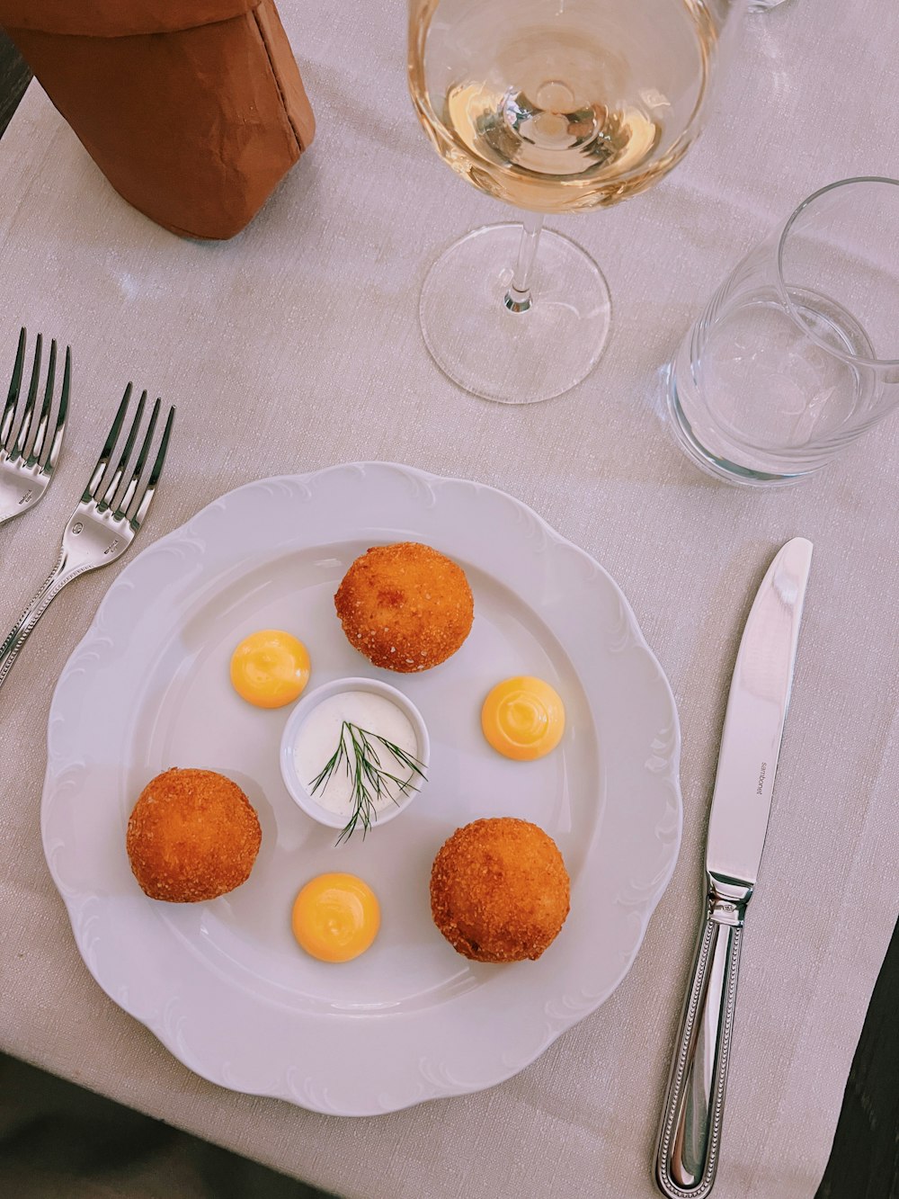 une assiette blanche garnie d’aliments frits à côté d’un verre de vin