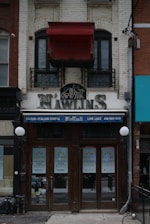 A two-story building with a brick facade featuring a storefront labeled 'N'awlins'. There are signs advertising 'Cajun - Italian Dining' and 'Live Jazz' with a phone number. The windows have 'For Lease' signs with contact details. A red canopy covers a balcony above.