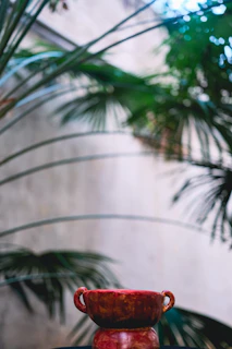 Close-up of a rich coral-colored ceramic bowl with visible finger grooves, resting next to fresh wildflowers in a sunlit kitchen.