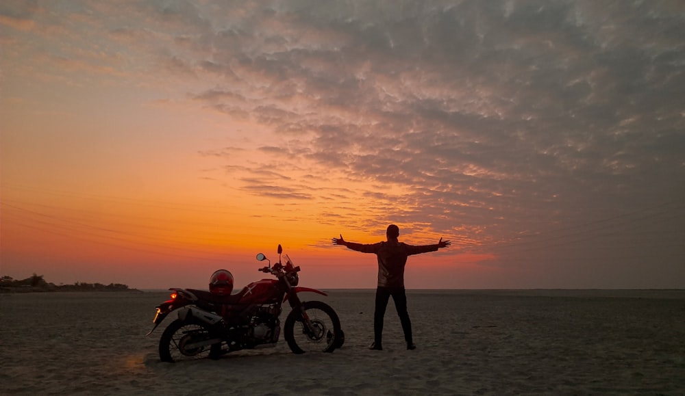 a man standing next to a motorcycle on a beach