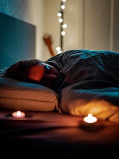 a person sleeping on a bed with some candles