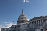 A large neoclassical building with a prominent dome and an American flag flying nearby, set against a clear blue sky.