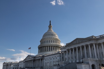 A large neoclassical building with a prominent dome and an American flag flying nearby, set against a clear blue sky.