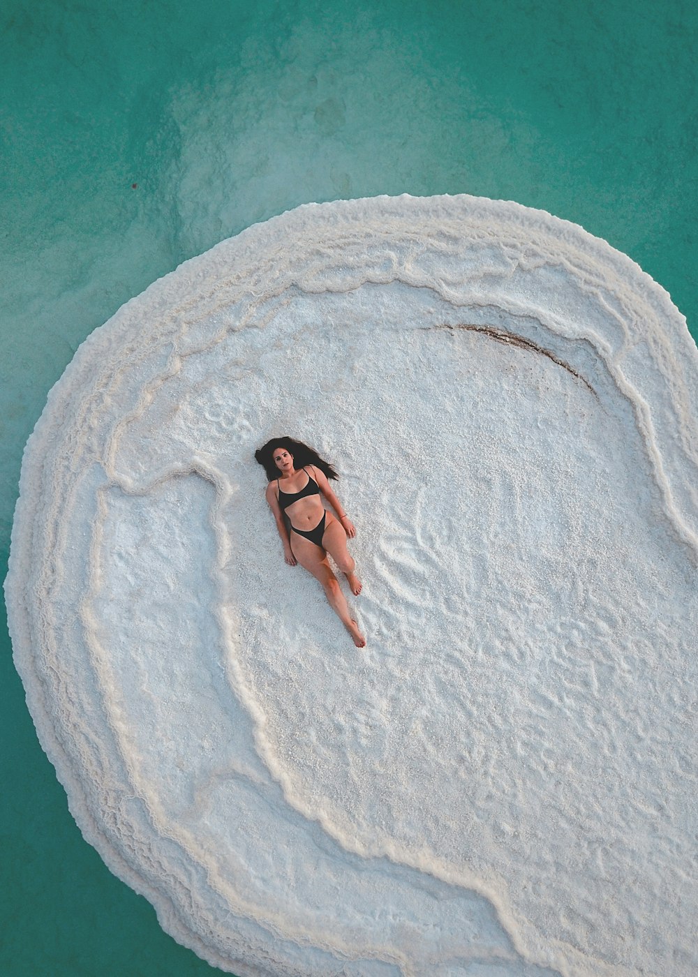 Una mujer en bikini negro acostada en una roca en el agua