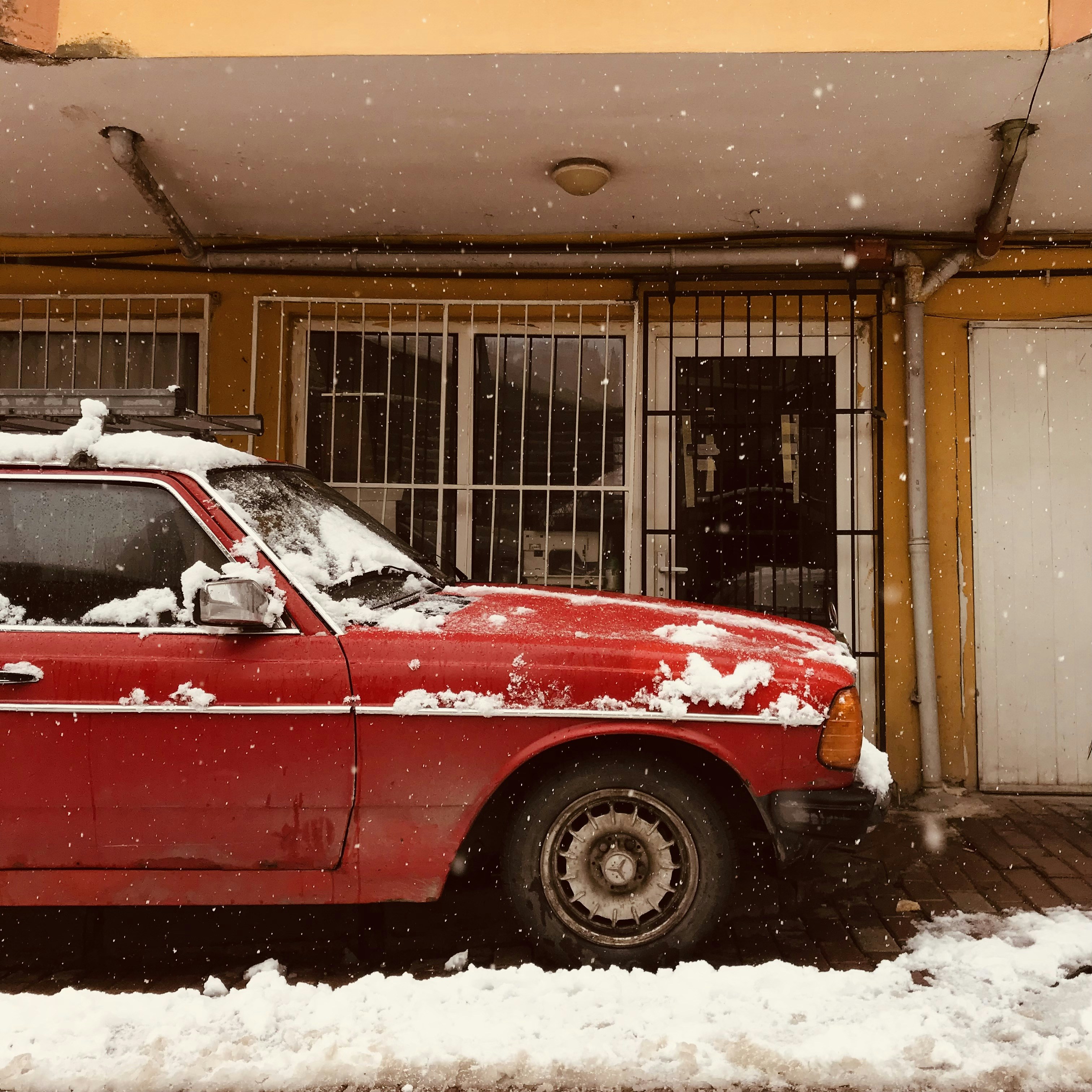 a red car parked in front of a building covered in snow