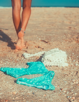 Model walking barefoot on the sand in a matching purple bikini and light aqua cover-up.