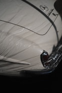 A classic car partially covered by a protective plastic wrap, showcasing a vintage design with a distinctive tail fin. The car is cream-colored with shiny chrome details and a recognizable emblem on the trunk.