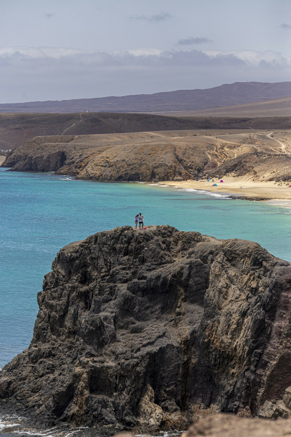 a couple of people standing on top of a cliff near the ocean