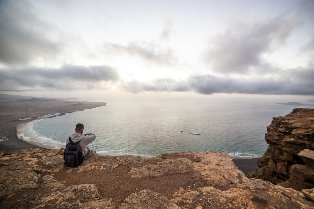 a man sitting on a cliff overlooking the ocean