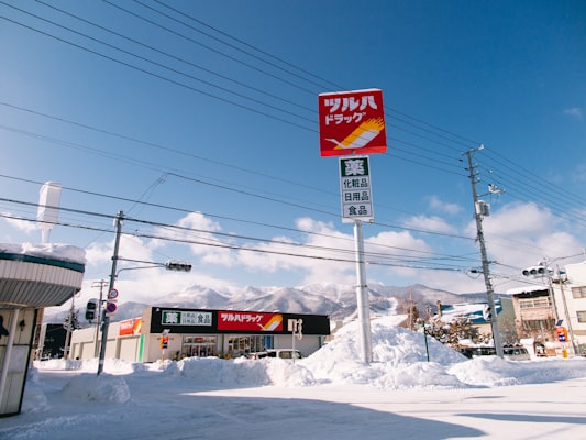 A snowbanked street in Furano town with a Tsuruha drugstore sign, power lines and snowy mountains in the distance