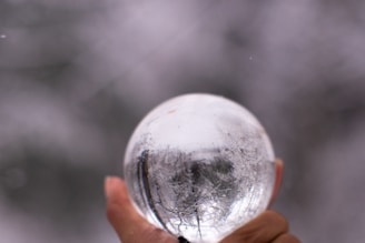A serene moment showing a person holding a large ice sphere formed with saunapearls mold, with steam rising softly in the background