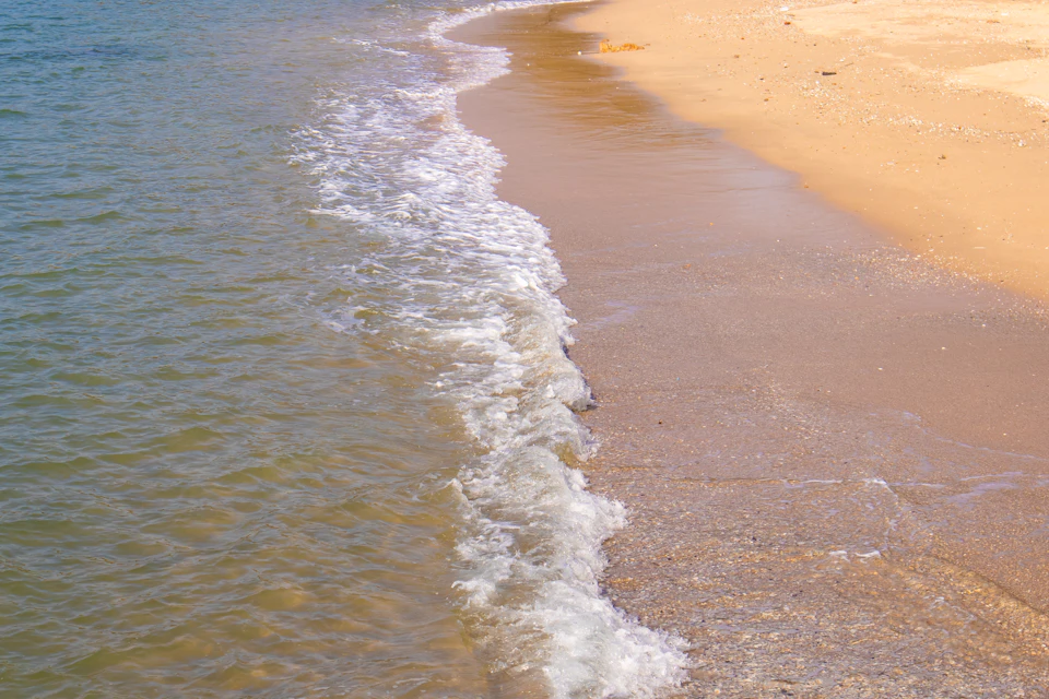 Serene beach scene with light beige sand and clear blue water in foreground