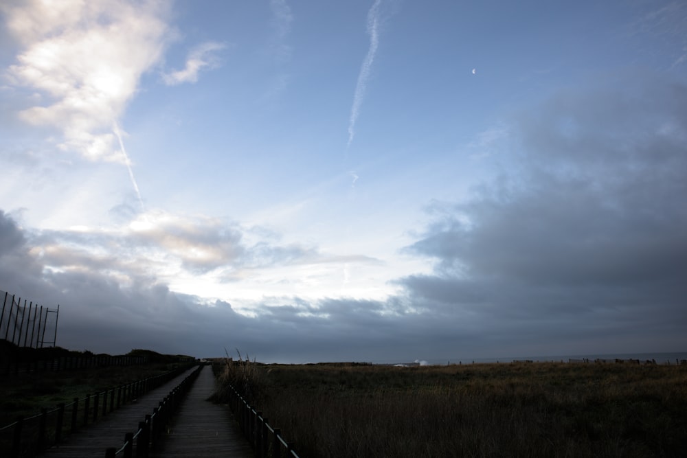 a boardwalk leading to a grassy field under a cloudy sky