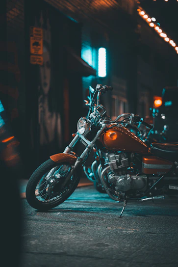 A vibrant photo capturing a classic Indian motorcycle gleaming under city lights with riders gearing up in neon-accented gear.