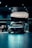 A sleek, modern black car is prominently displayed in a dimly lit showroom with spotlights highlighting its design. The showroom features a polished tiled floor and contemporary furnishings.