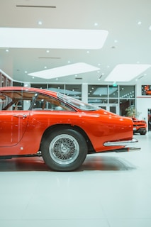 A shiny red vintage car parked inside Khan Motors showroom, reflecting the warm showroom lights.