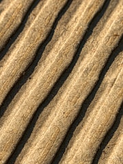 Close-up view of corrugated cardboard with parallel ridges and a textured surface in an earthy beige color.