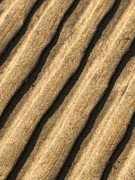 Close-up view of corrugated cardboard with parallel ridges and a textured surface in an earthy beige color.