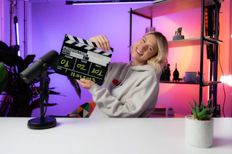 a woman sitting at a table holding a movie clapper
