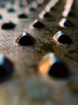 Close-up view of a metallic surface with an array of pyramid-shaped protrusions. The image focuses on the textures and patterns of the surface with shallow depth of field, creating a blurred background.