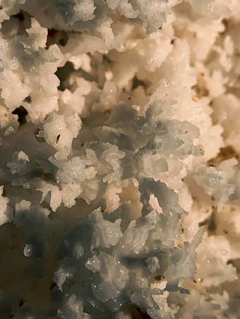 Close-up view of crystalline or grainy textured material with irregular shapes and varying shades of white, blue, and beige.