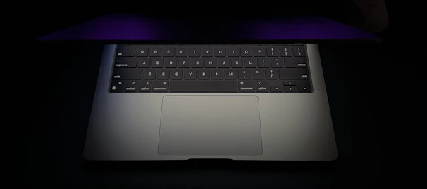 A user typing on a backlit keyboard of a laptop with a sleek, dark gray chassis.