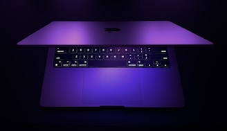 A laptop with a purple backlit keyboard in a dimly lit room.
