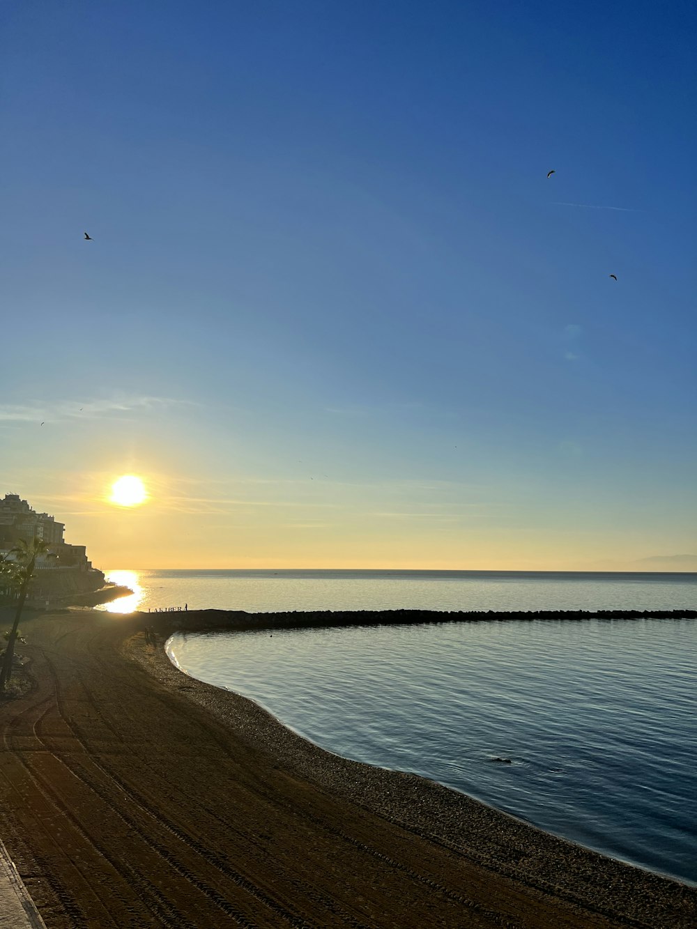 the sun is setting over the water at the beach