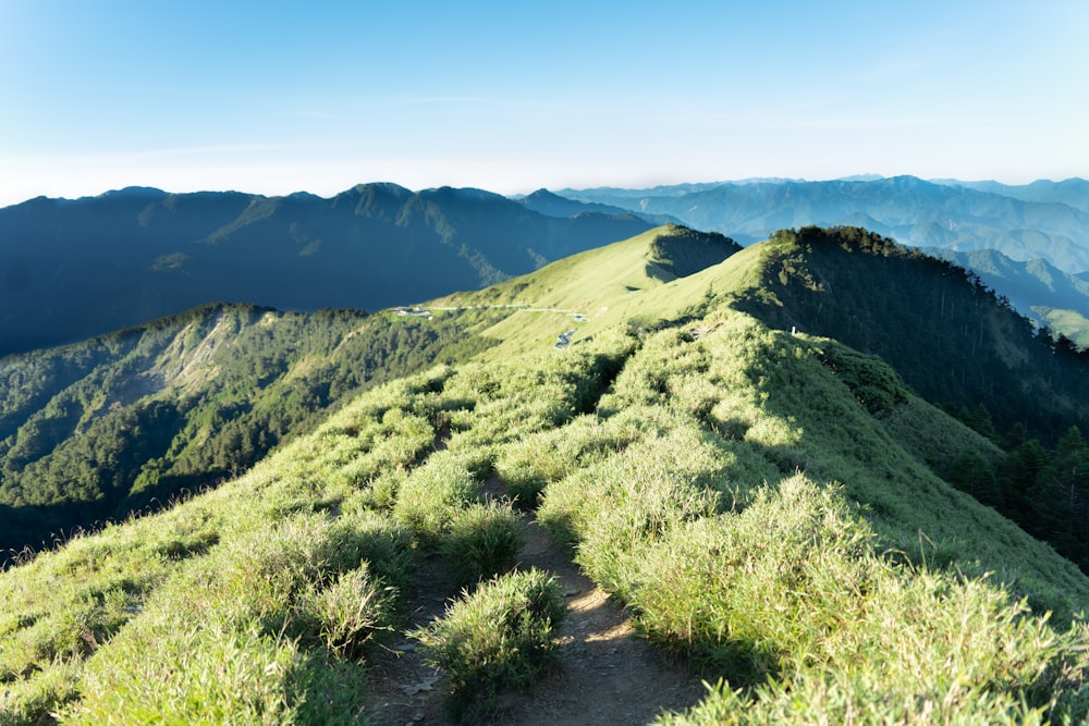 a trail going up a grassy hill with mountains in the background