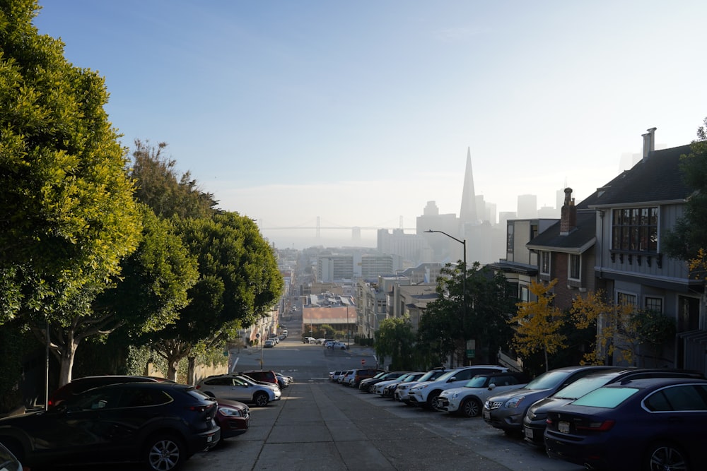 a street lined with parked cars in front of a city skyline