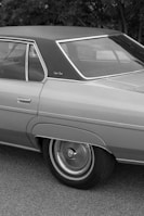 A classic car features prominently, showcasing its distinct design elements such as the sleek roofline and chrome accents. The black and white photo highlights the smooth curves and detailed hubcaps of the vehicle.
