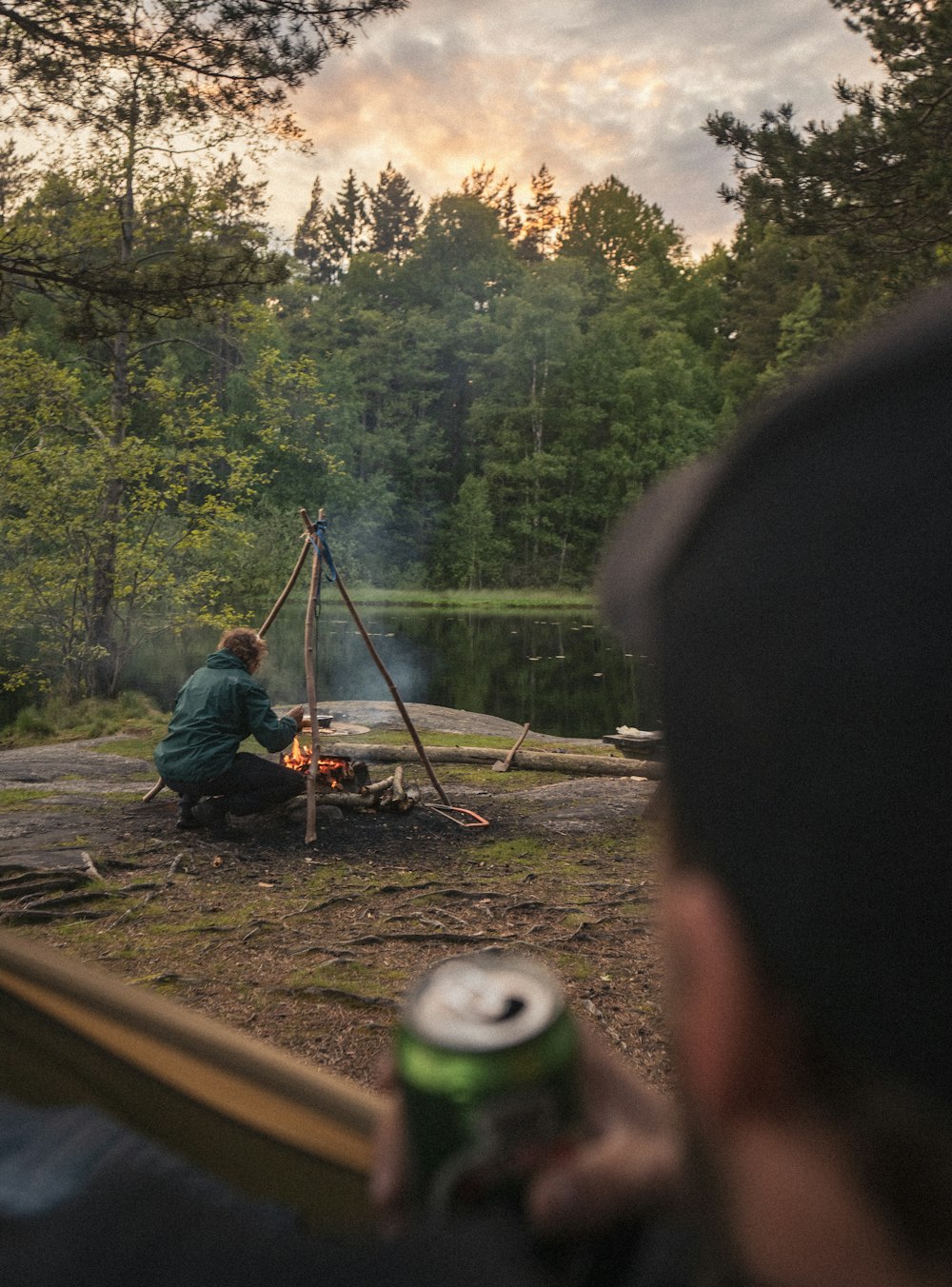 a man sitting at a campfire with a beer