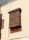 A traditional wooden lattice window protrudes from a beige wall. The intricate geometric patterns and carvings on the window are accentuated by the warm sunlight. The structure showcases heritage architectural elements with its detailed craftsmanship.