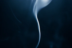 Soft smoke swirling in the air above a dark charcoal surface, illuminated by subtle golden light