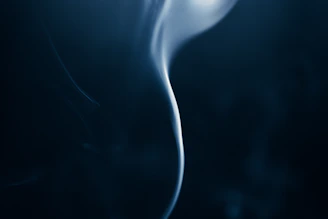 Soft smoke swirling in the air above a dark charcoal surface, illuminated by subtle golden light