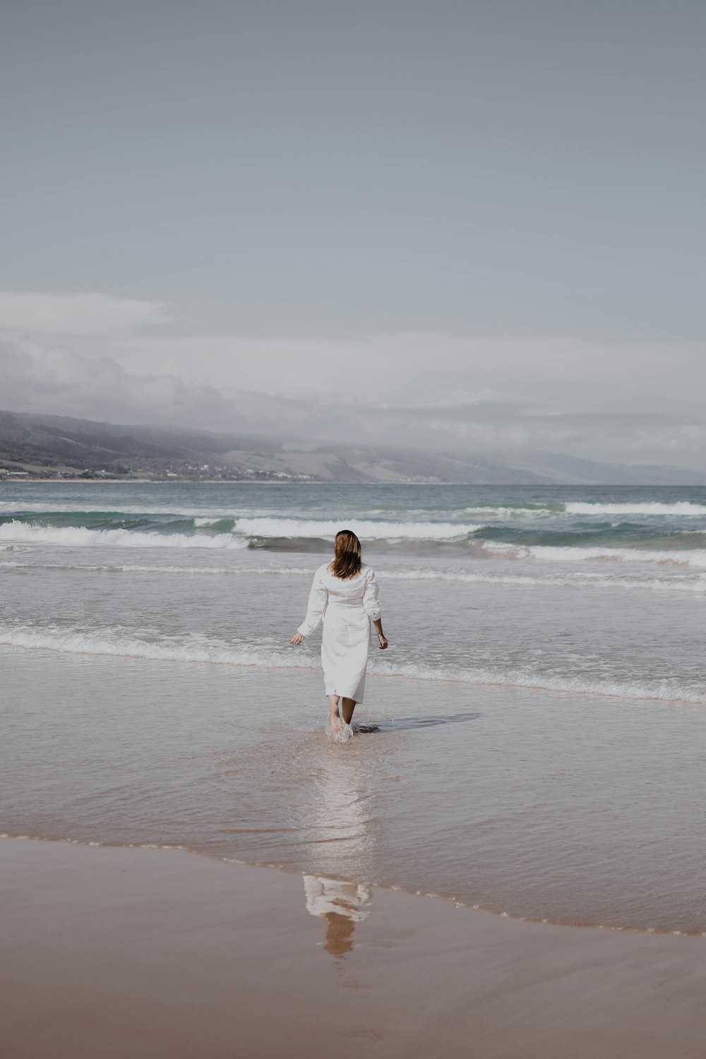 Eine Frau in einem weißen Kleid spaziert am Strand