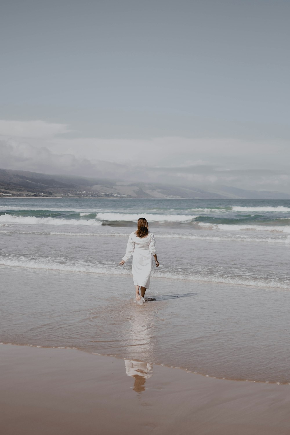 a woman in a white dress walking on the beach