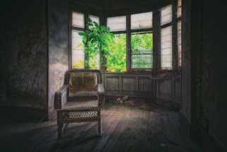 Un fauteuil vintage trône dans une pièce sombre et délabrée au sol recouvert de parquet. La pièce es