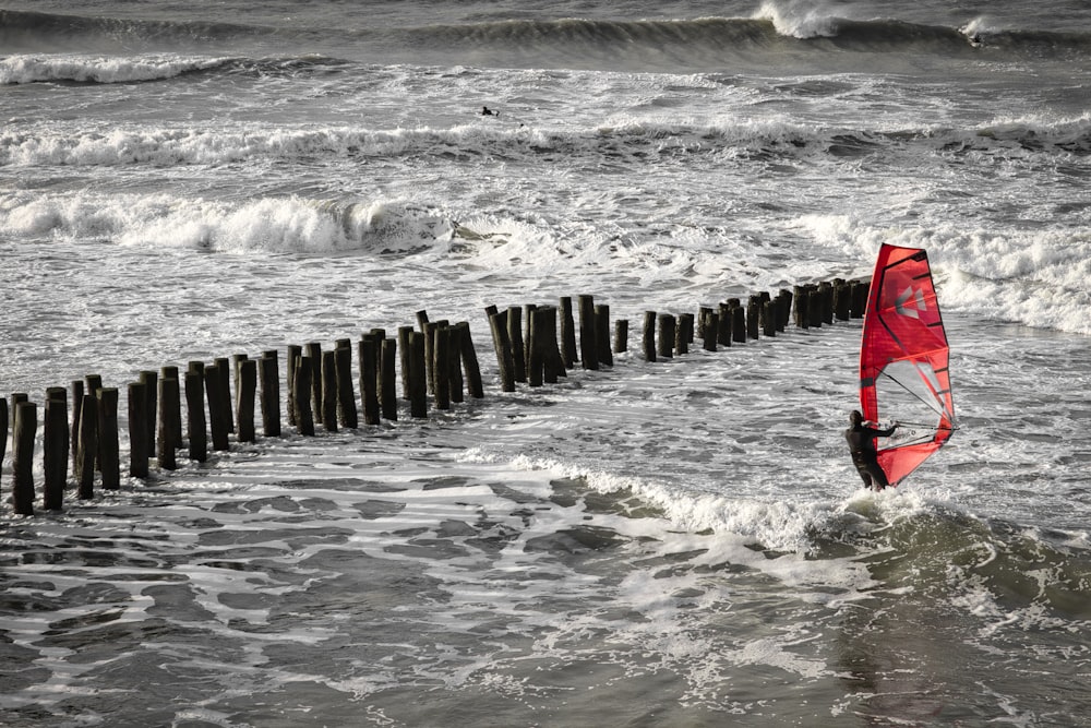 a red surfboard sitting on top of a wooden post in the ocean