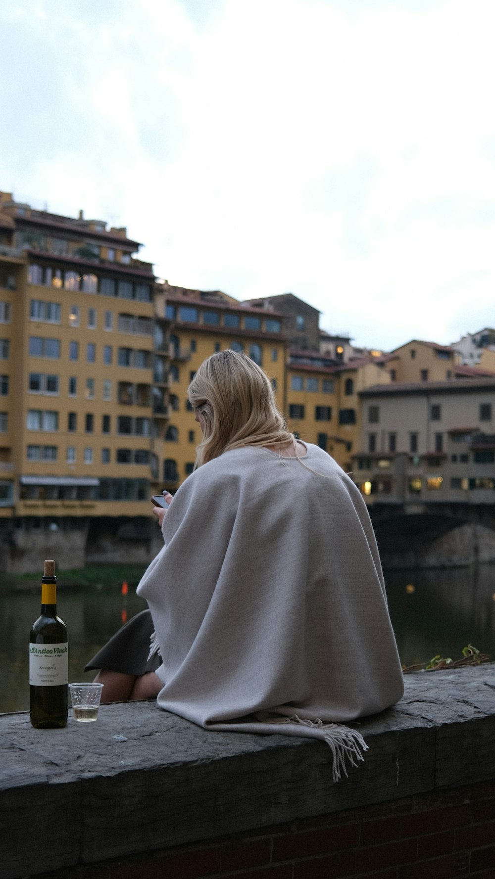 a woman sitting on a ledge with a bottle of wine